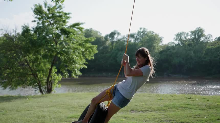 A woman swings on a tire swing next to a lake