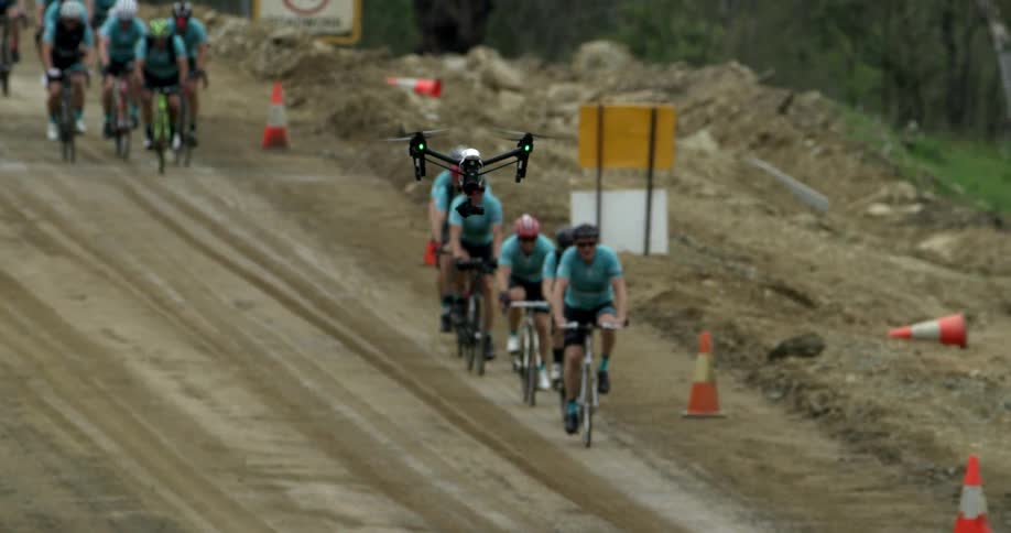 A drone flies near a line of cyclists