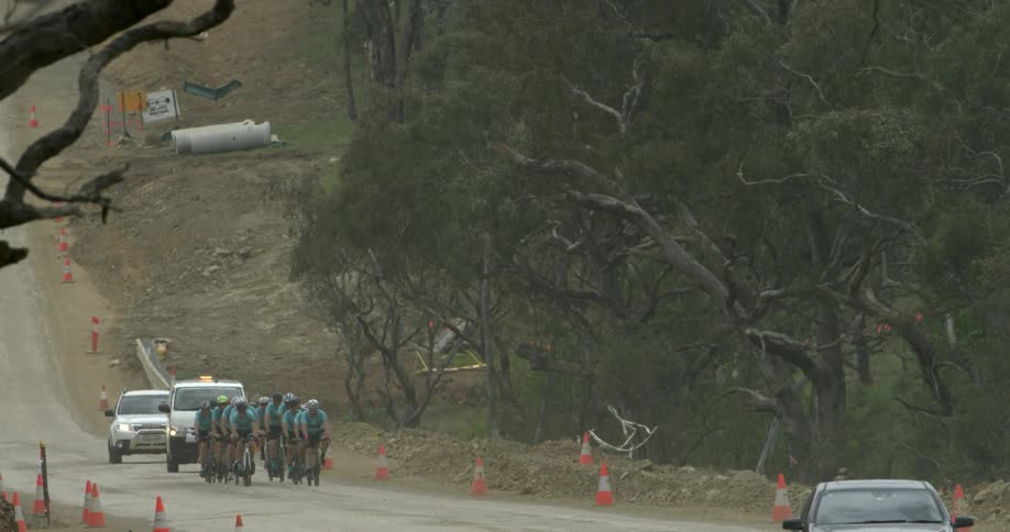 A line of cyclists riding in front of a flashing truck