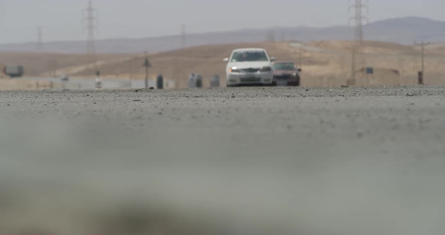 Vehicles and trucks travel along a desert road during the day