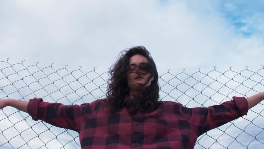 A woman leans against a chain link fence
