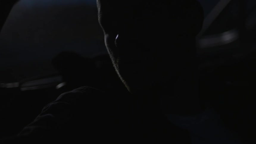 A man sits in a dark car at night