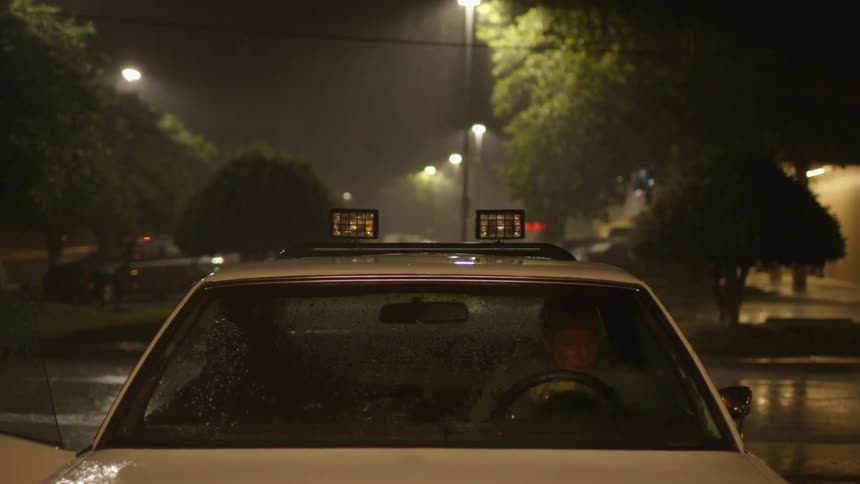 A young man gets into a car on a rainy night
