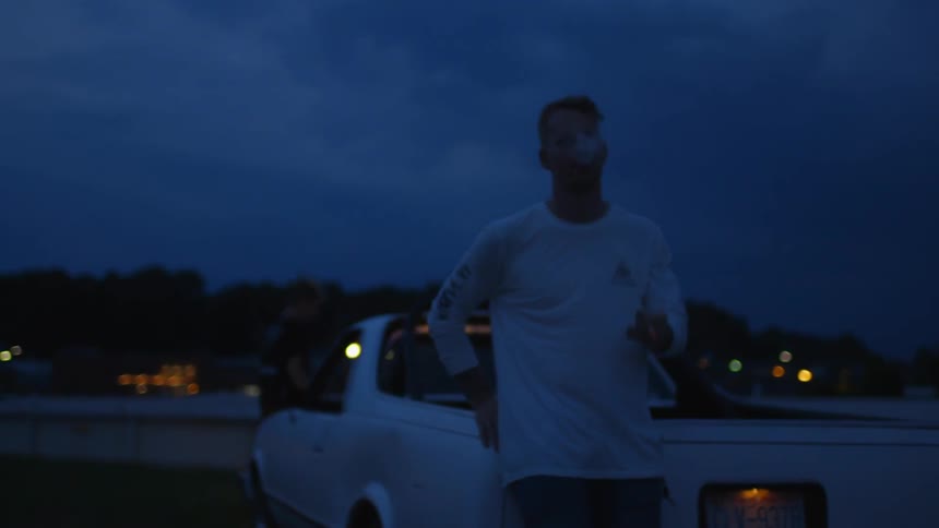 A man smokes a cigarette while leaning against a truck at night
