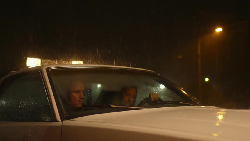 Two people sit in a car in the rain