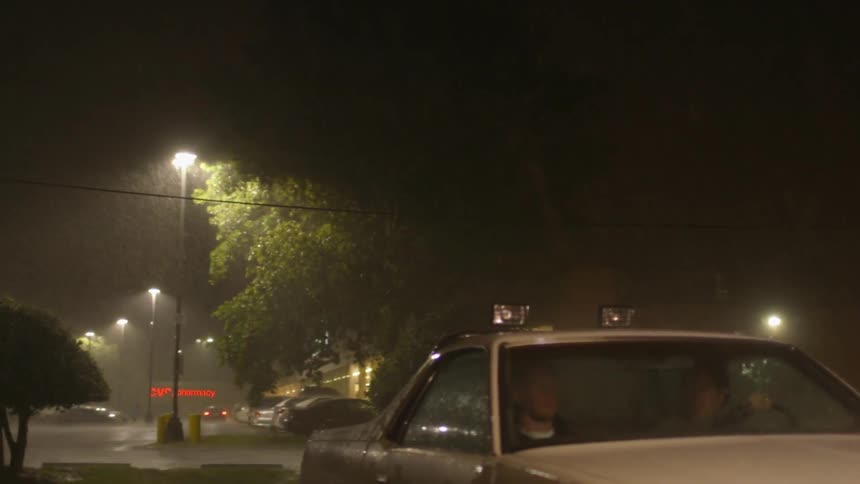 People sit in a car as it rains and lightning flashes in the night sky