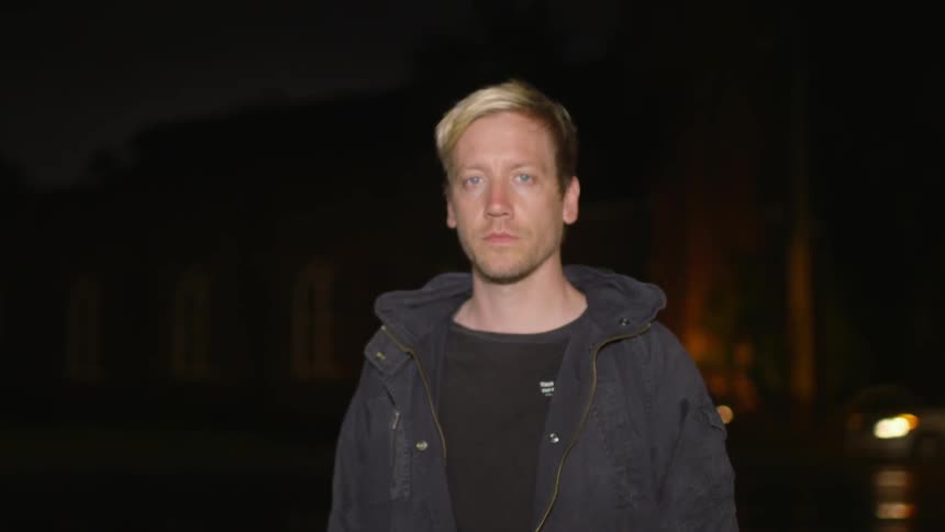 A man stands next to a street at night