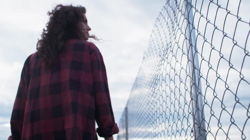 A woman is walking near a chain link fence during the day