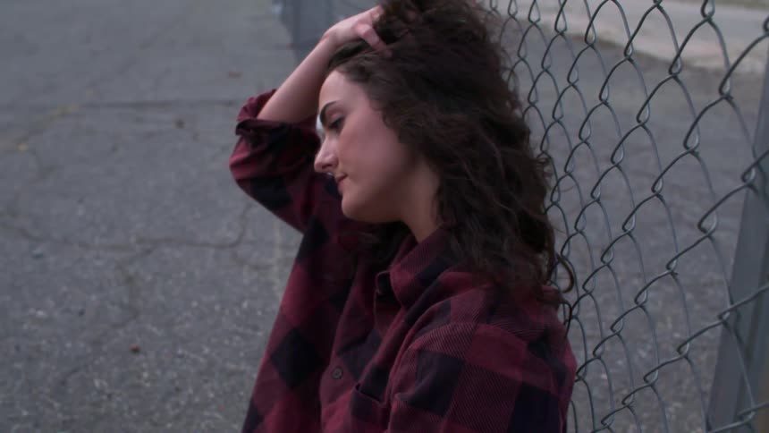 A woman sits on the asphalt against a fence
