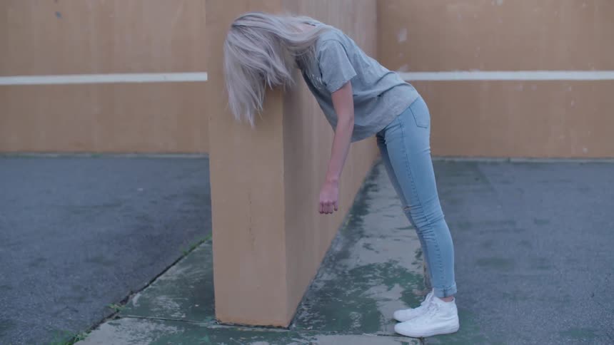 A woman leans against a wall outside