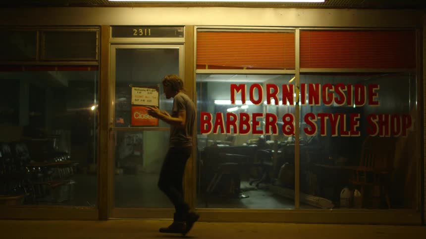 A man dances in front of a closed barbershop