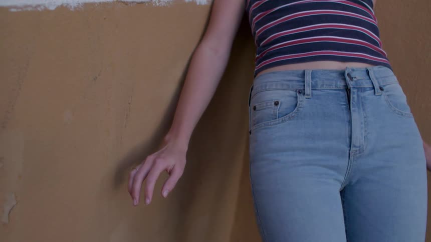 A woman moves her hand down along a wall she is leaning on