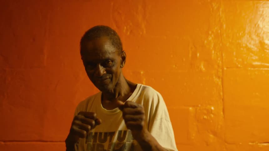 An elderly man holds up his fists outside at night