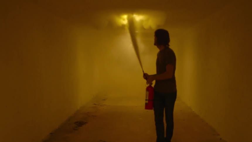 A man uses a fire extinguisher inside an empty hallway