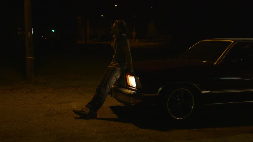 A man leans against the hood of a parked car