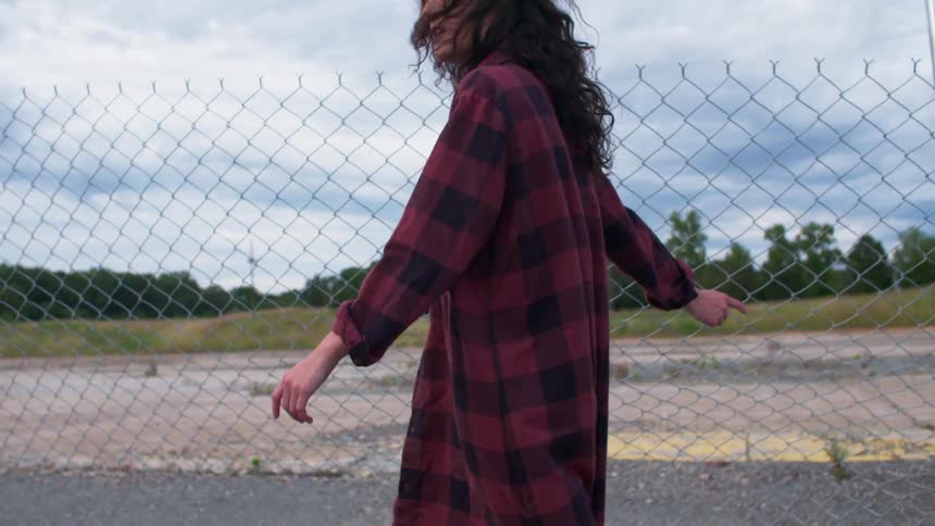 A woman is walking along a fence touching it along the way
