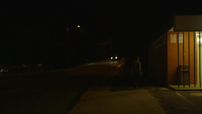 A man walks by a brick building at night
