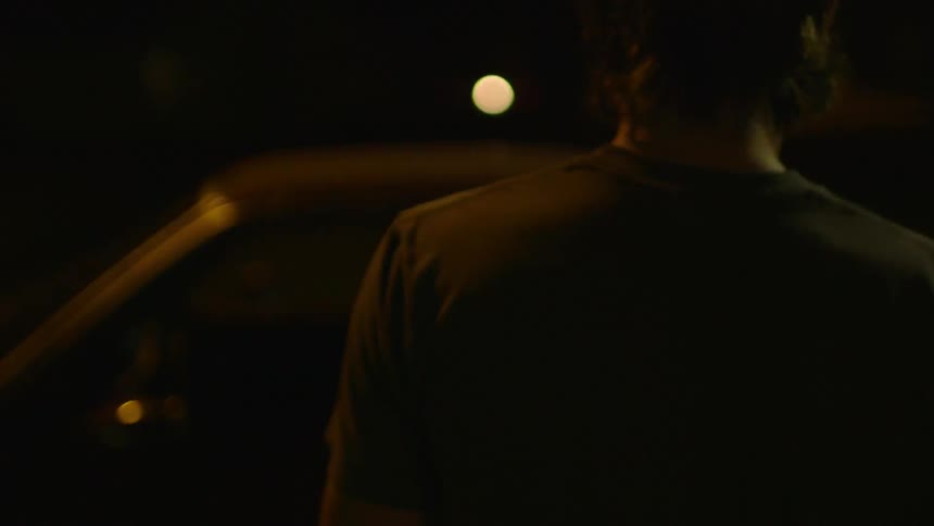 A young man walks to and enters a car at night