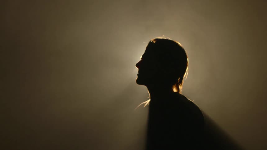 A person looks down in a dark foggy room