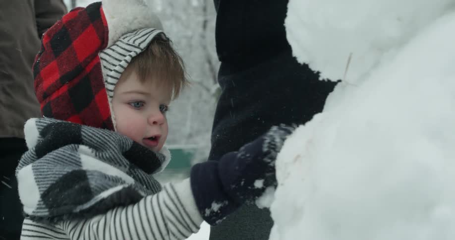 A toddler pats a snowman near his parents