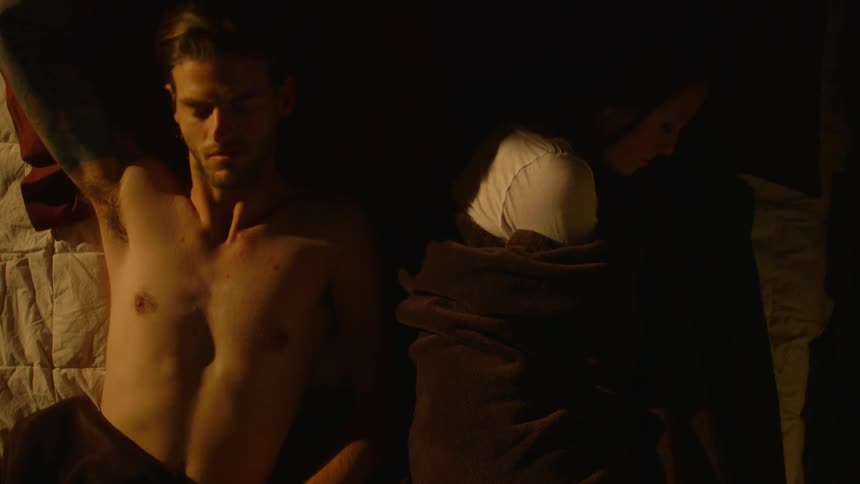 A shirtless man lies beside a sleeping woman