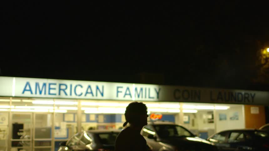 A man smokes in front of a laundromat