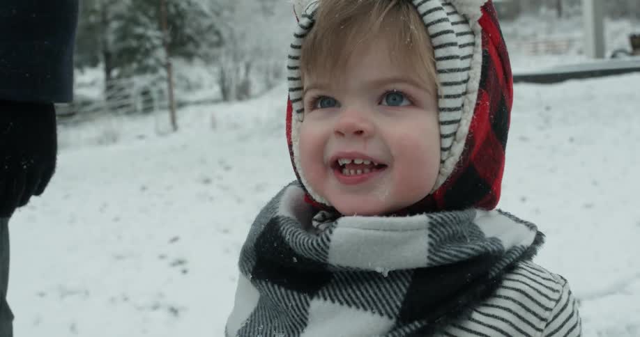 A toddler boy smiles as he stands outside in the snow