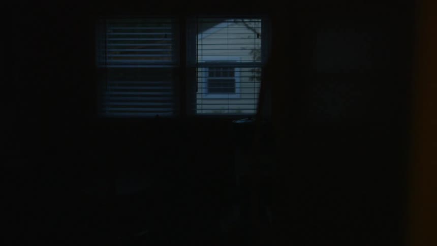 The dark room has a window with the blinds open