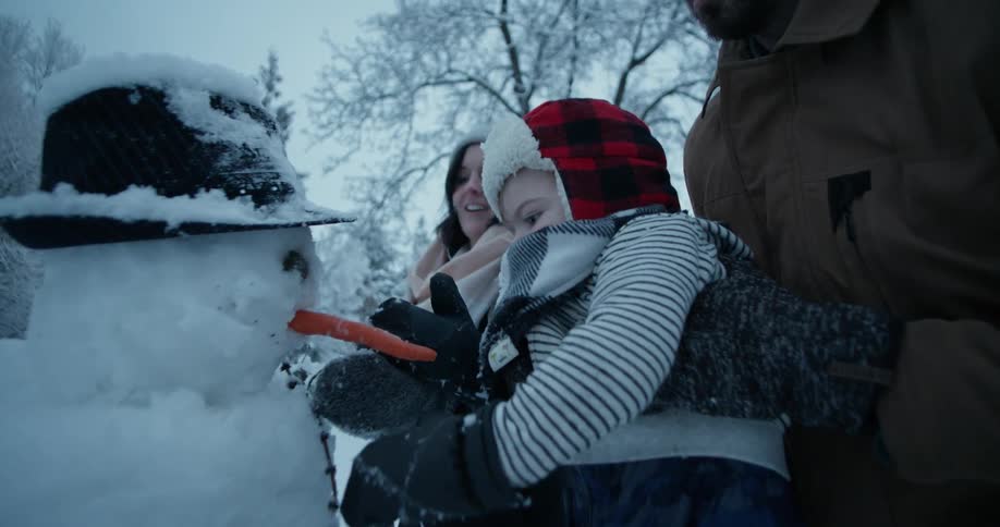 Parents help a child put the nose on a snowman