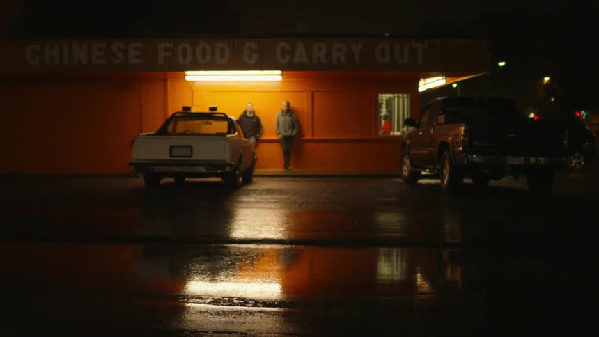 Two people are standing against a building while its raining at night