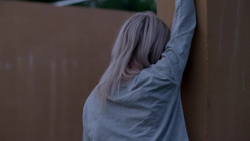 A woman leans up against a wall outside