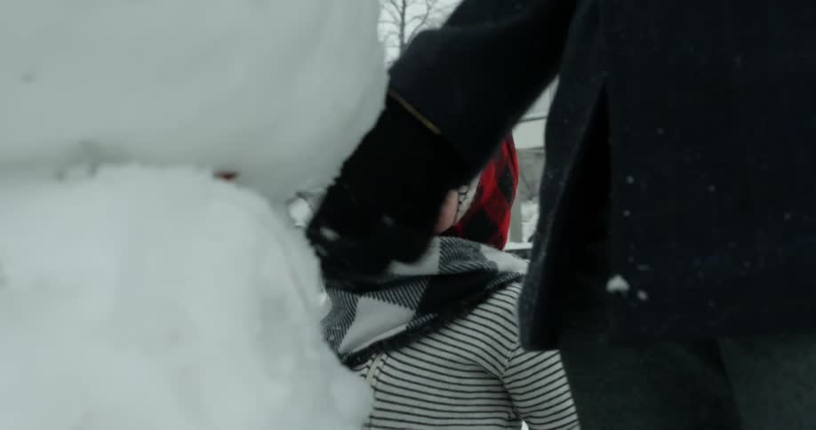 A young child stands next to a built snowman