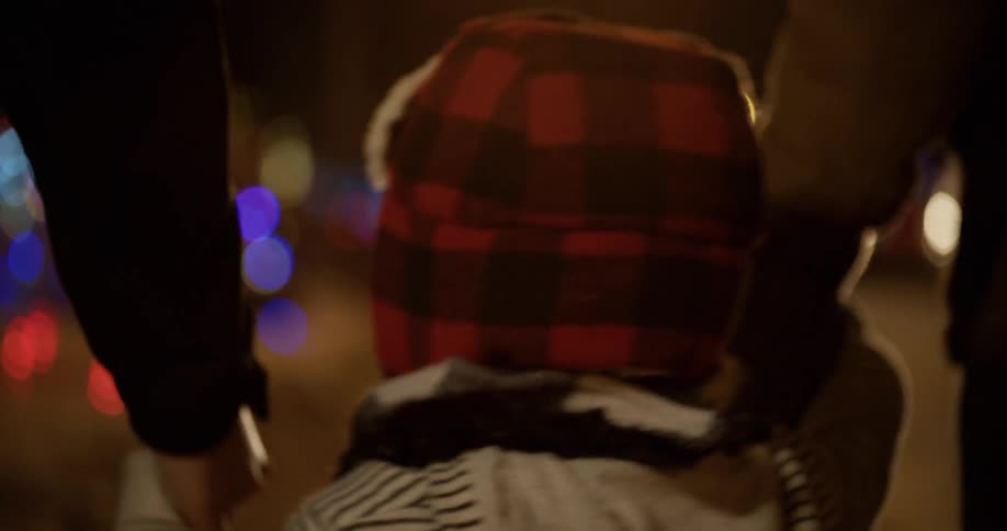 A boy smiles as he walks holding hands with his parents at night