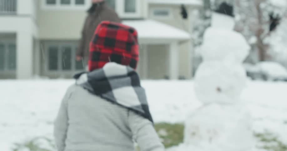 A child runs up to a snowman