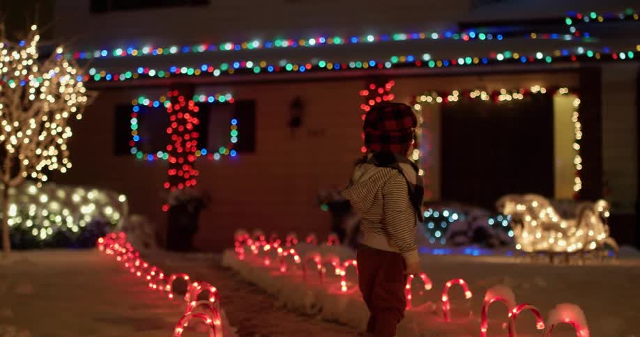 A boy walks towards a home brightly lit with christmas decorations