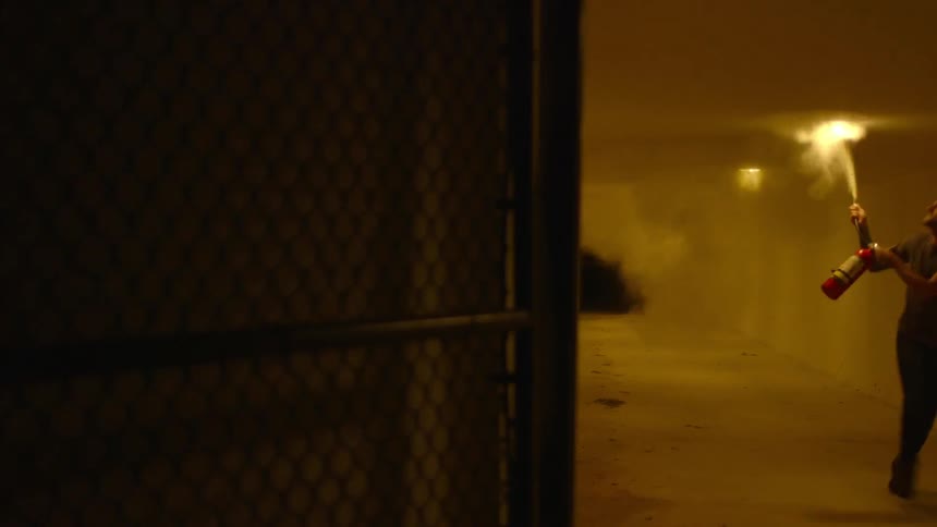 A man sprays a fire extinguisher in a corridor