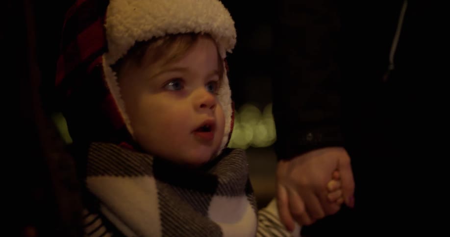 A young boy points at christmas lights at night