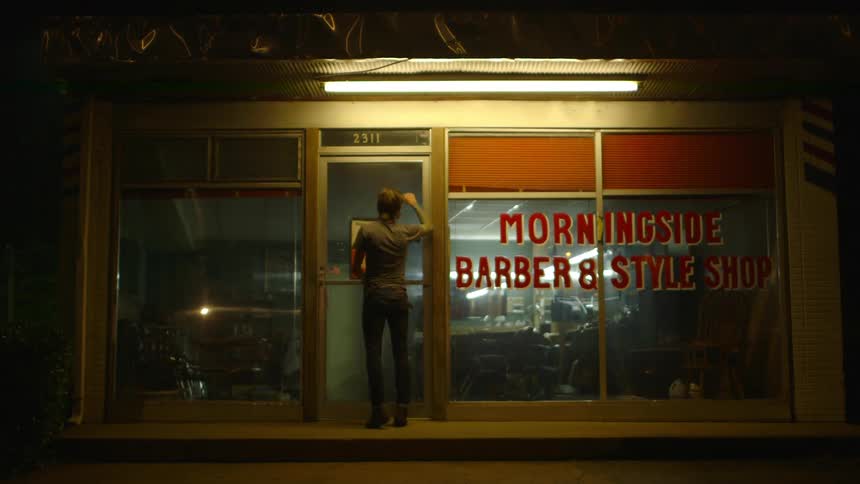 A man knocks on a closed barbershop door at night