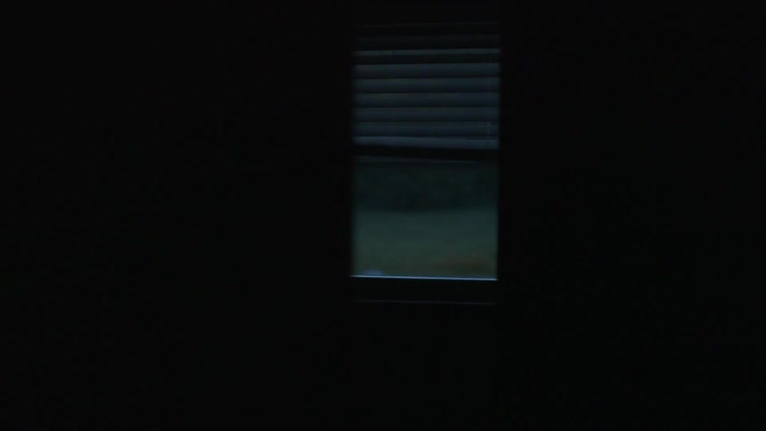 Blinds hang in a window as someone turns off the light