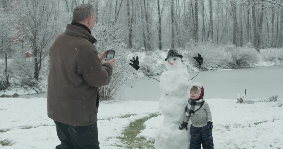 A man takes a photo of a child next to a snowman
