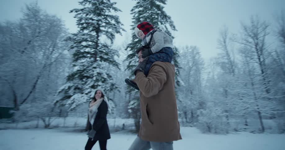 A man carries a young boy through the snow on his shoulders