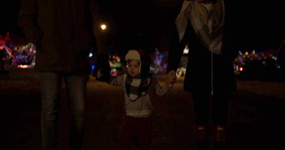 Young child walks as he holds hands with a man and woman