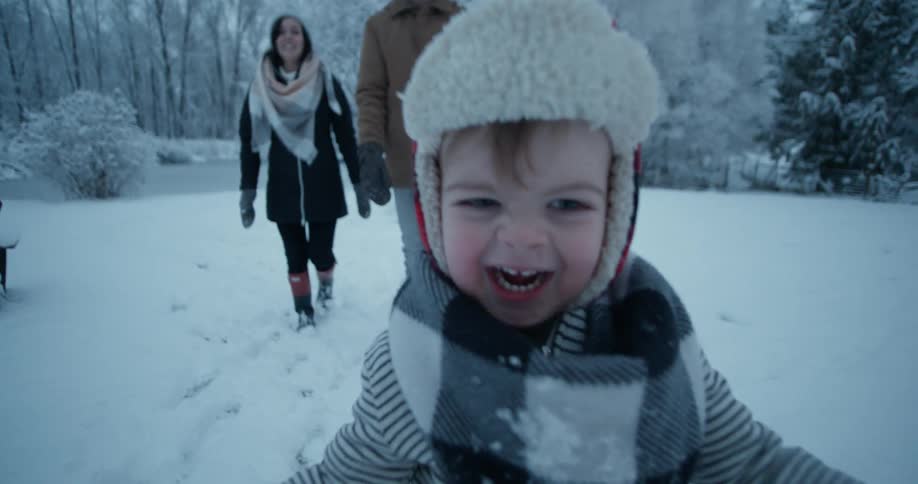 Two adults and a small child are running and smiling through snow