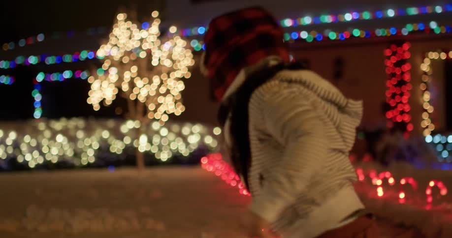 Child walking outside at night in front of a house lit up with lights
