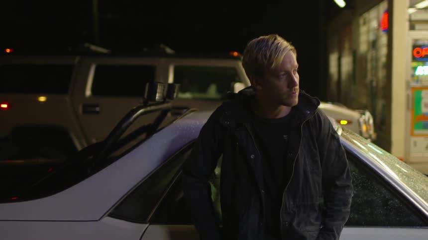 A man leans against a car in a parking lot