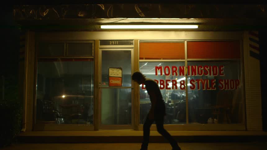 A man walks past a shop at night and lays down in the street