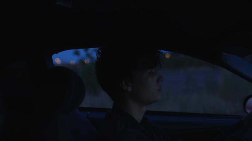 Young man sits in a car as he moves his hand through his hair