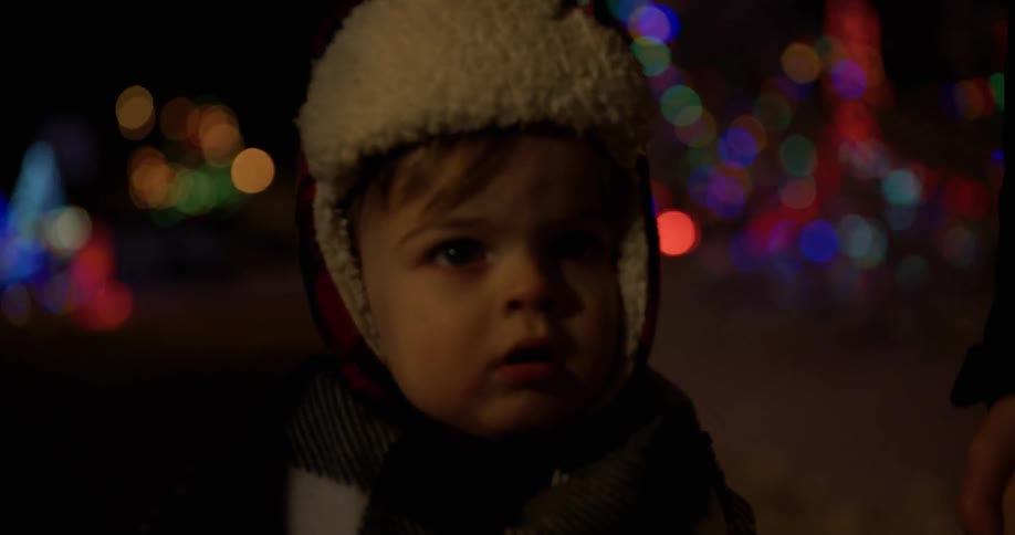 A young child is walking past christmas lights at night