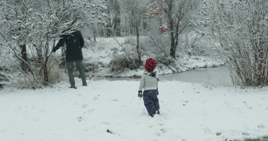 Young child walks in the snow towards a man near a tree