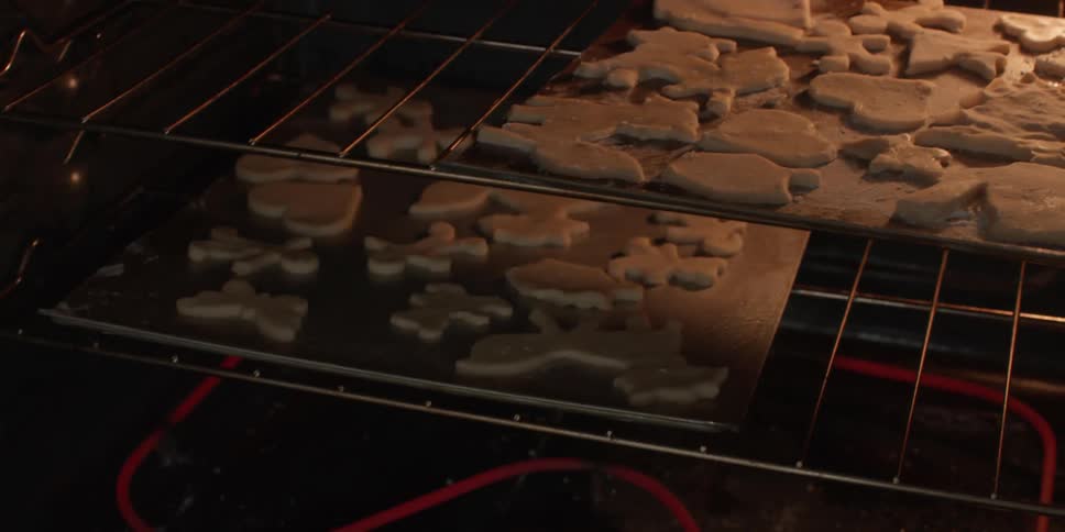 A person puts sheets full of cookies into the oven to bake